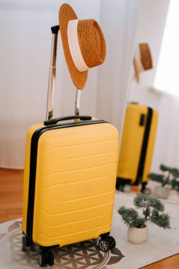 Yellow suitcase and straw hat ready for an exciting vacation trip in a modern indoor setting clipart