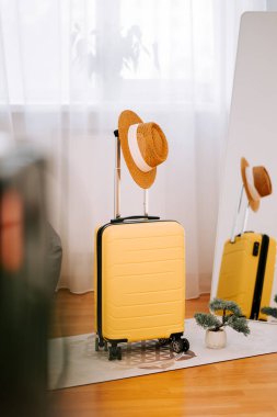 Sarı bavul ve hasır şapka modern bir ev ortamında heyecan verici bir tatil gezisine hazır.