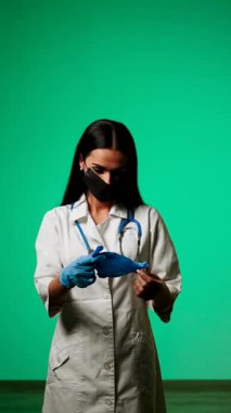Klinik ortamda yeşil bir zemine karşı maske ve steteskop takan sağlık uzmanı