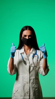 Klinik ortamda yeşil bir zemine karşı maske ve steteskop takan sağlık uzmanı