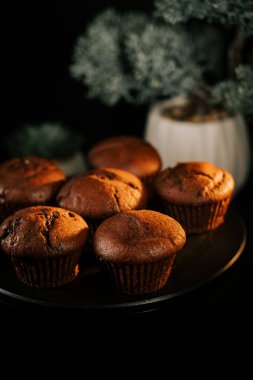 Taze pişmiş çikolatalı kekler yeşil bitkilerle çevrili siyah bir tabakta sergilenir.