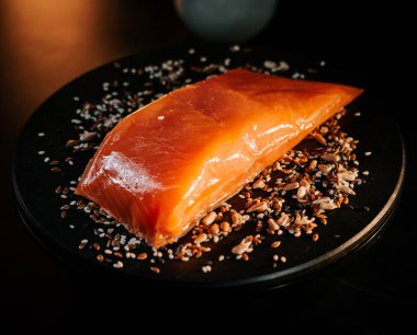 Tohumlarla çevrili siyah servis tahtasındaki taze organik alabalık filetosu.