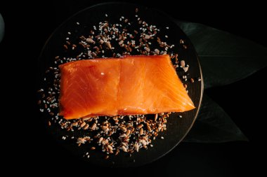 Tohumlarla çevrili siyah servis tahtasındaki taze organik alabalık filetosu.