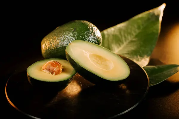 Taze avokado ikiye bölünmüş kremsi yeşil et ve büyük tohumu siyah arka planda sergiliyor.