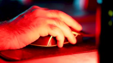 Gece vakti loş bir oyun ayarında oyun faresi kullanan bir elin yakın plan görüntüsü