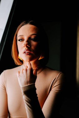 Model, yaratıcı bir moda çekimi sırasında minimalist bir stüdyoda canlı turuncu şapkayla dramatik bir şekilde poz verir.