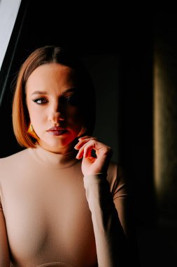 Model, yaratıcı bir moda çekimi sırasında minimalist bir stüdyoda canlı turuncu şapkayla dramatik bir şekilde poz verir.