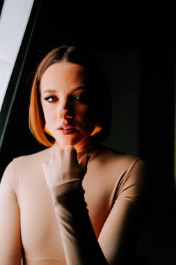 Model, yaratıcı bir moda çekimi sırasında minimalist bir stüdyoda canlı turuncu şapkayla dramatik bir şekilde poz verir.