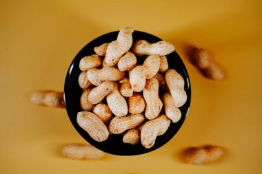 Canlı bir atıştırmalık sunumu için parlak sarı arka planda siyah bir kasede taze toplanmış fıstıklar.