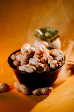 Canlı bir atıştırmalık sunumu için parlak sarı arka planda siyah bir kasede taze toplanmış fıstıklar.