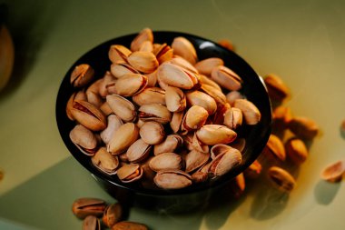 Yeşil arka planda siyah bir kasede taze kabuklu fıstıklar, canlı dokularını ve doğal cazibelerini sergiliyorlar.