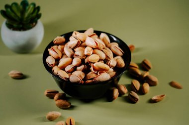 Yeşil arka planda siyah bir kasede taze kabuklu fıstıklar, canlı dokularını ve doğal cazibelerini sergiliyorlar.