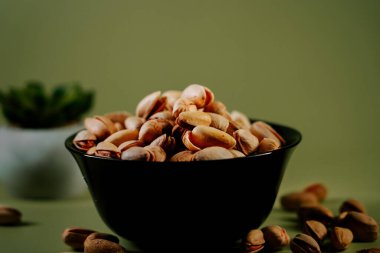 Yeşil arka planda siyah bir kasede taze kabuklu fıstıklar, canlı dokularını ve doğal cazibelerini sergiliyorlar.