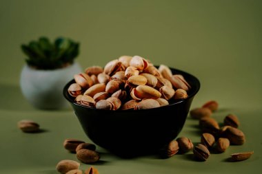 Yeşil arka planda siyah bir kasede taze kabuklu fıstıklar, canlı dokularını ve doğal cazibelerini sergiliyorlar.