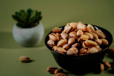 Yeşil arka planda siyah bir kasede taze kabuklu fıstıklar, canlı dokularını ve doğal cazibelerini sergiliyorlar.