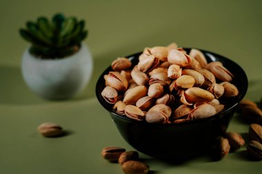Yeşil arka planda siyah bir kasede taze kabuklu fıstıklar, canlı dokularını ve doğal cazibelerini sergiliyorlar.