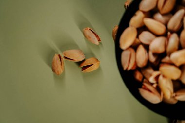 Yeşil arka planda siyah bir kasede taze kabuklu fıstıklar, canlı dokularını ve doğal cazibelerini sergiliyorlar.