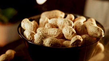 Siyah arka planda dönen tabakta yer fıstıkları. Akşam saatlerinde yerel bir markette yakın çekimde lezzetli kavrulmuş fıstık sergilendi.