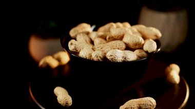 Siyah arka planda dönen tabakta yer fıstıkları. Akşam saatlerinde yerel bir markette yakın çekimde lezzetli kavrulmuş fıstık sergilendi.