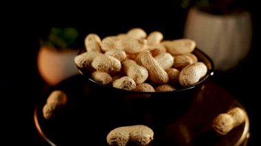 Siyah arka planda dönen tabakta yer fıstıkları. Akşam saatlerinde yerel bir markette yakın çekimde lezzetli kavrulmuş fıstık sergilendi.