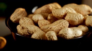 Siyah arka planda dönen tabakta yer fıstıkları. Akşam saatlerinde yerel bir markette yakın çekimde lezzetli kavrulmuş fıstık sergilendi.