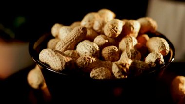 Siyah arka planda dönen tabakta yer fıstıkları. Akşam saatlerinde yerel bir markette yakın çekimde lezzetli kavrulmuş fıstık sergilendi.