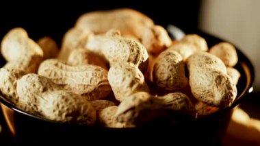 Siyah arka planda dönen tabakta yer fıstıkları. Akşam saatlerinde yerel bir markette yakın çekimde lezzetli kavrulmuş fıstık sergilendi.