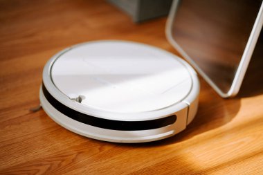 Robot elektrikli süpürge modern oturma odasındaki ahşap zeminde gündüz vakti doğal ışıkla çalışıyor.
