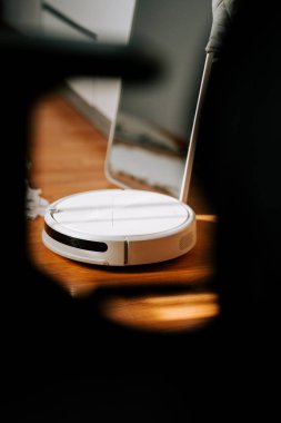 Robot elektrikli süpürge modern oturma odasındaki ahşap zeminde gündüz vakti doğal ışıkla çalışıyor.