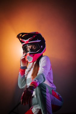 Miğferli bir kadın motosikletçinin portresi. Gece parlak neon ışıklarıyla aydınlatılıyor.