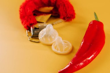 Kırmızı biber, prezervatif ve parlak sarı arka planda eğlenceli aksesuarlar.