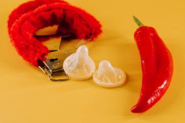 Kırmızı biber, prezervatif ve parlak sarı arka planda eğlenceli aksesuarlar.