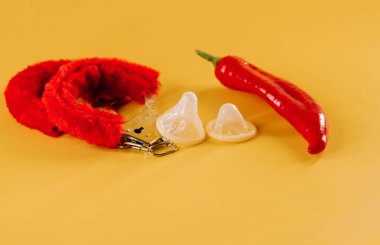 Kırmızı biber, prezervatif ve parlak sarı arka planda eğlenceli aksesuarlar.