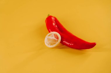 Kırmızı biber, prezervatif ve parlak sarı arka planda eğlenceli aksesuarlar.