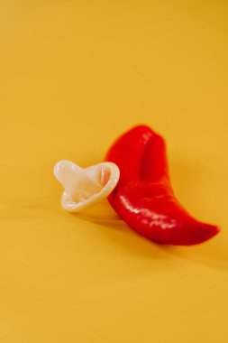 Kırmızı biber, prezervatif ve parlak sarı arka planda eğlenceli aksesuarlar.