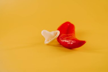 Kırmızı biber, prezervatif ve parlak sarı arka planda eğlenceli aksesuarlar.