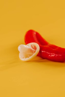 Kırmızı biber, prezervatif ve parlak sarı arka planda eğlenceli aksesuarlar.