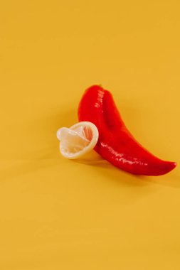 Kırmızı biber, prezervatif ve parlak sarı arka planda eğlenceli aksesuarlar.