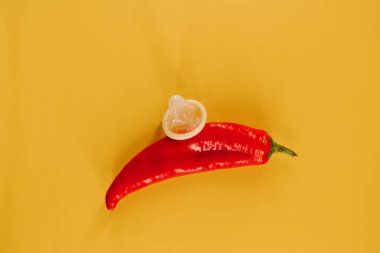 Kırmızı biber, prezervatif ve parlak sarı arka planda eğlenceli aksesuarlar.