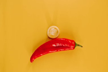 Kırmızı biber, prezervatif ve parlak sarı arka planda eğlenceli aksesuarlar.