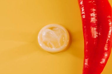 Kırmızı biber, prezervatif ve parlak sarı arka planda eğlenceli aksesuarlar.