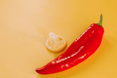 Kırmızı biber, prezervatif ve parlak sarı arka planda eğlenceli aksesuarlar.