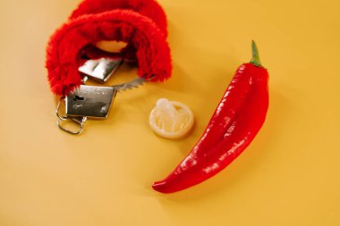 Kırmızı biber, prezervatif ve parlak sarı arka planda eğlenceli aksesuarlar.