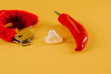 Kırmızı biber, prezervatif ve parlak sarı arka planda eğlenceli aksesuarlar.