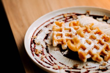 Lezzetli Belçika waffleları, meyve sosu ve fındıklı dekoratif bir tabakta servis edilir.