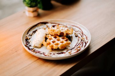 Muz dilimleri ve şurupla dekoratif bir tabakta servis edilen lezzetli Belçika waffleları.