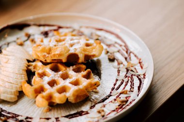 Sıcak bir kafede dilimlenmiş muz ve fındıkla servis edilen lezzetli Belçika waffle 'ları.
