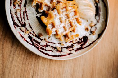Tatmin edici Belçika waffleları. Tahta bir masada dondurma ve meyve sosuyla servis ediliyor.