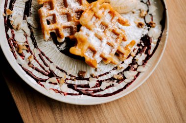 Lezzetli Belçika waffleları, rahat bir kafe ortamında soslu ve süslü bir tabakta servis edilir.