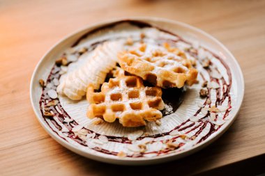 Lezzetli Belçika waffleları taze muz dilimleri ve sıcak bir kafede çilek yağmuru ile servis edilir.